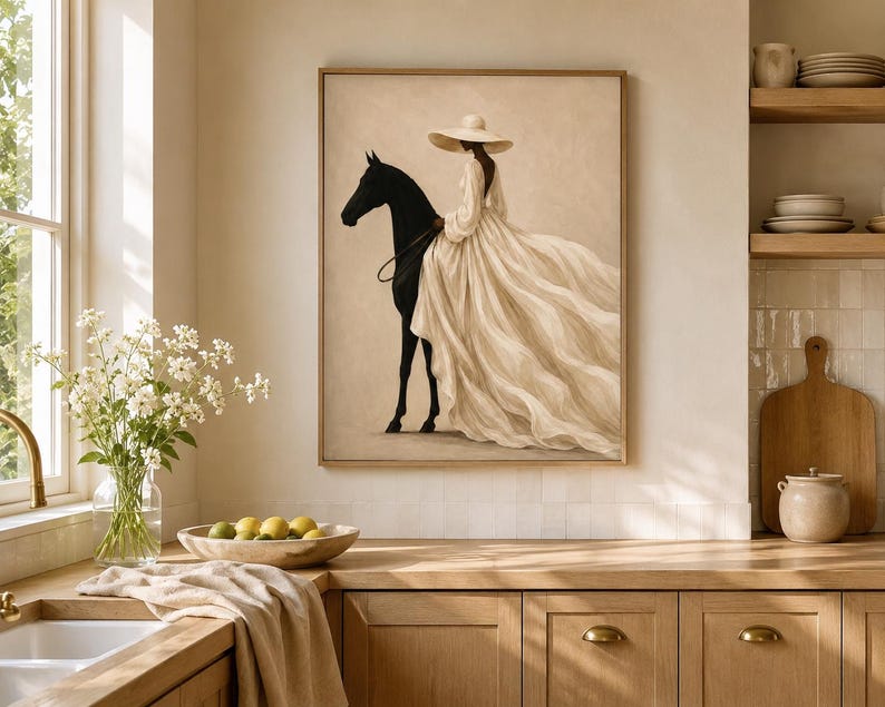 May include: A framed wall art print featuring a silhouette of a black horse and a figure wearing a wide-brimmed hat and a long, flowing cream-colored dress. The artwork is rendered in a neutral color palette with soft beige and cream tones.