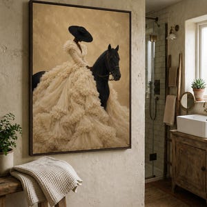 May include: A framed wall art print featuring a person wearing a wide-brimmed black hat and a voluminous, layered cream-colored ruffled gown, riding a black horse against a textured, muted tan background. The artwork is displayed in a dark frame.