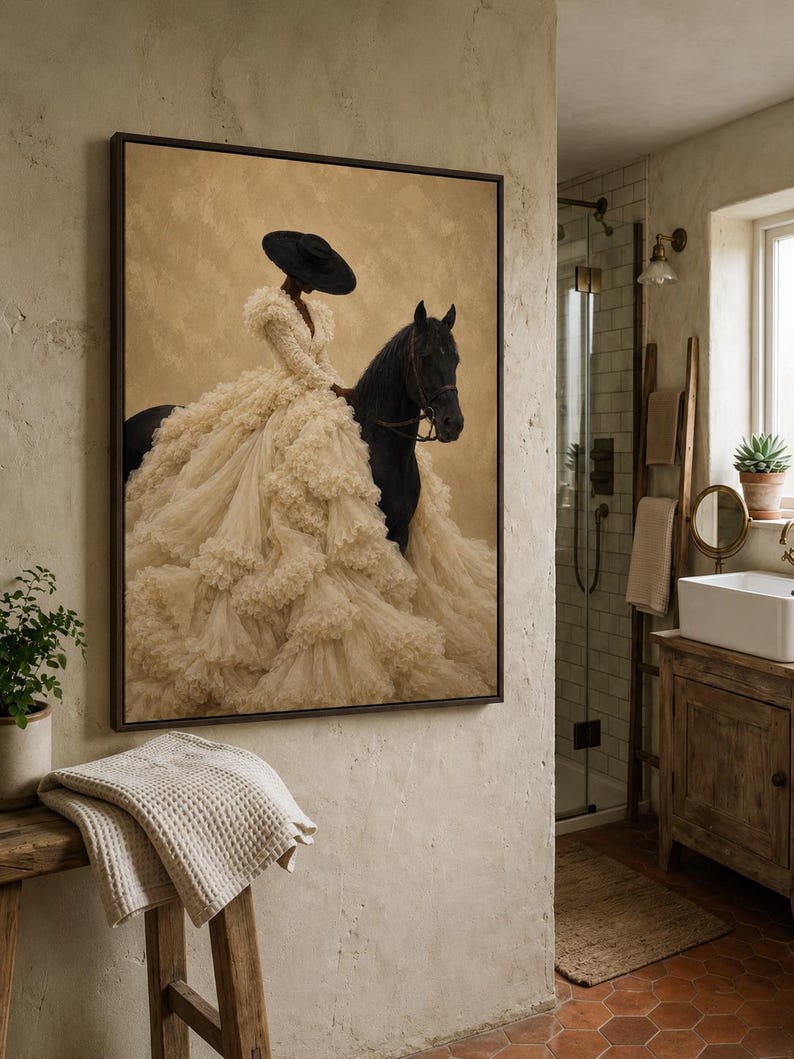 May include: A framed wall art print featuring a person wearing a wide-brimmed black hat and a voluminous, layered cream-colored ruffled gown, riding a black horse against a textured, muted tan background. The artwork is displayed in a dark frame.
