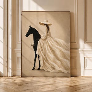 May include: A framed wall art print depicting a figure wearing a wide-brimmed hat and a long, flowing cream-colored gown while standing beside a solid black horse. The artwork features a neutral beige background and soft, diffused lighting.