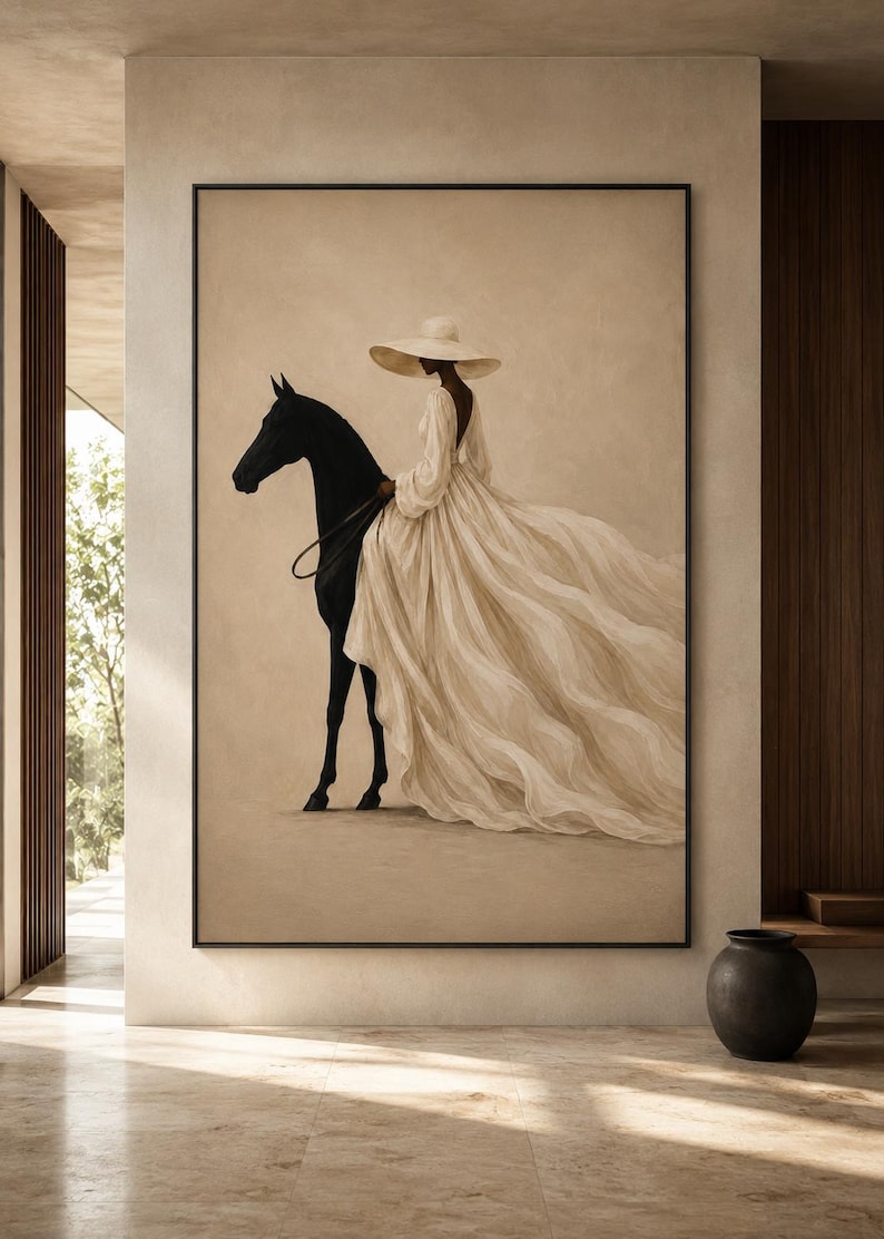 May include: A framed wall art print featuring a side profile of a black horse and a figure wearing a wide-brimmed hat and a long, flowing cream-colored dress with a deep back neckline. The artwork is displayed on a neutral-toned wall.