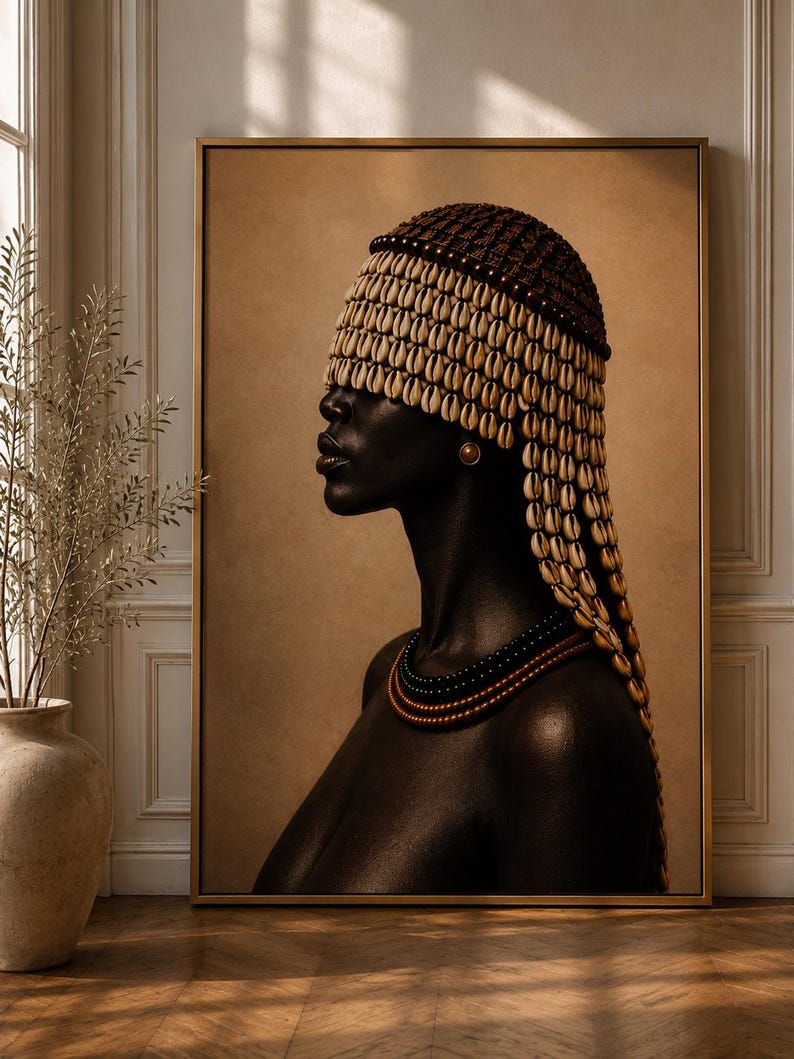 May include: A framed wall art print depicting a profile portrait of a person with dark skin wearing a headpiece covered in rows of cream-colored cowrie shells and a multi-layered beaded necklace in black and copper tones against a tan background.