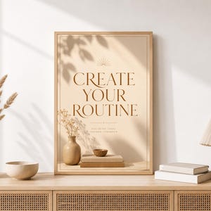Puede incluir: Una lámina de arte enmarcada con fondo beige que presenta el texto "CREATE YOUR ROUTINE" en fuente serif marrón oscuro, con un texto más pequeño debajo que dice "DISCIPLINE TODAY FREEDOM TOMORROW" y un pequeño icono de sol.