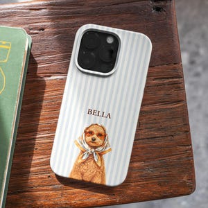 May include: A phone case with a light blue and white striped pattern. The case features a graphic of a poodle wearing sunglasses and a scarf. The name "BELLA" is printed above the poodle.