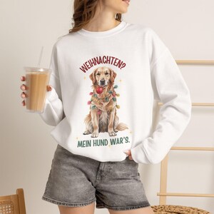 Könnte beinhalten: Ein weißes Langarm-Sweatshirt mit einer Grafik eines Golden Retrievers, der in bunte Lichterketten gewickelt ist und eine rote Kugel im Maul hält. Der Text darüber lautet WEIHNACHTEN? und der Text darunter MEIN HUND WAR'S.