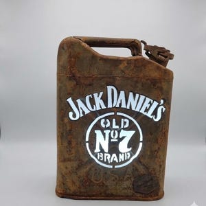 Könnte beinhalten: Ein rostbrauner Metallkanister mit dem Jack Daniel's Old No. 7 Brand Logo in Weiß. Der Kanister hat einen Griff und einen Ausguss, und das Logo ist beleuchtet.