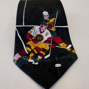 May include: Black necktie with a hockey-themed design featuring two hockey players in action. The players are wearing jerseys with the letters "B" and "C" on them. The tie has a black background with a paisley pattern.