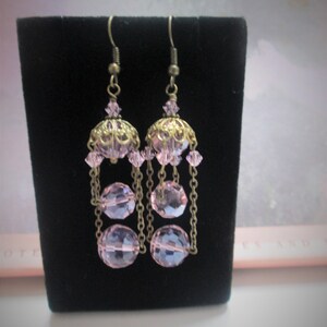 May include: A pair of dangle earrings with a pink crystal charm and multiple pink crystal beads hanging from a gold chain.