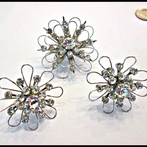 May include: Three silver flower-shaped brooches with clear rhinestones.