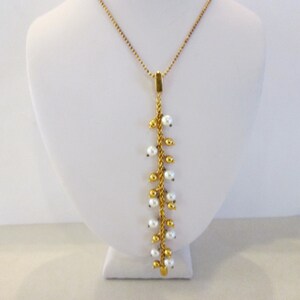 May include: A gold-toned necklace with a delicate chain and a vertical strand of small, white pearls. The pearls are interspersed with gold beads, creating a cascading effect. The necklace is displayed on a white bust.