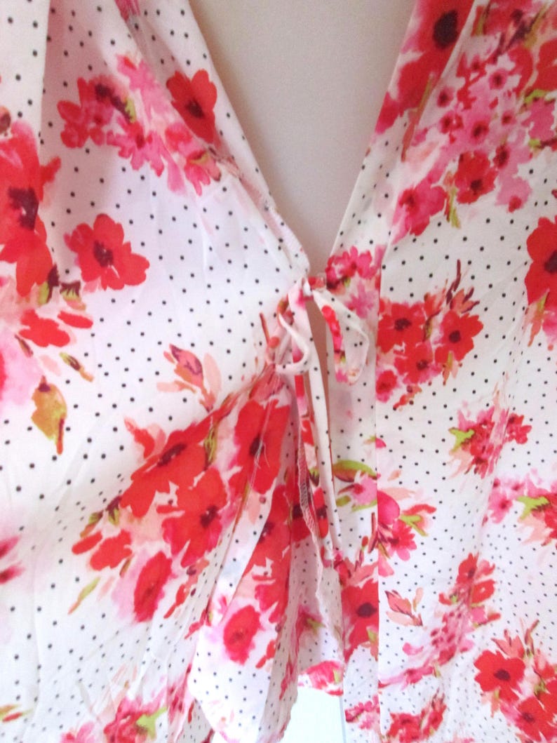 May include: A white blouse with a floral pattern of red and pink flowers. The blouse has a polka dot design and a tie closure at the neckline. The fabric appears to be lightweight and flowy.