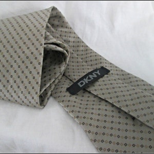 May include: A beige patterned tie with a black and brown diamond pattern. The tie has a black label with the text "DKNY" on it.