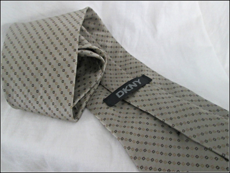 May include: A beige patterned tie with a black and brown diamond pattern. The tie has a black label with the text "DKNY" on it.