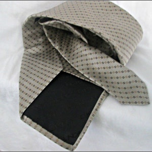May include: A beige silk tie with a brown and black geometric pattern. The tie is folded in half and the back side is visible.