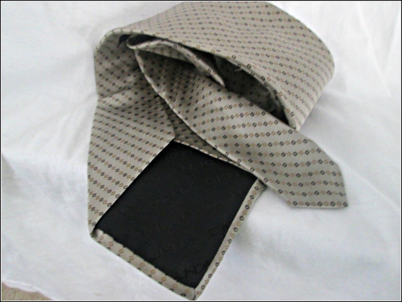 May include: A beige silk tie with a brown and black geometric pattern. The tie is folded in half and the back side is visible.