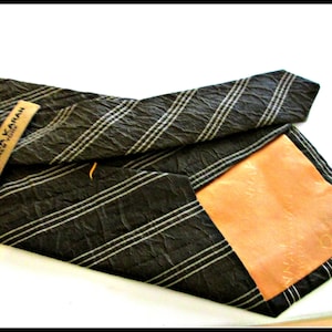 May include: A black and white striped tie with a brown textured fabric. The tie has a brown leather label with the text "DONNA KARAN NEW YORK" printed on it.