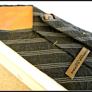 May include: A black and white striped tie with a brown leather patch and a black label that reads "DONNA KARAN NEW YORK".