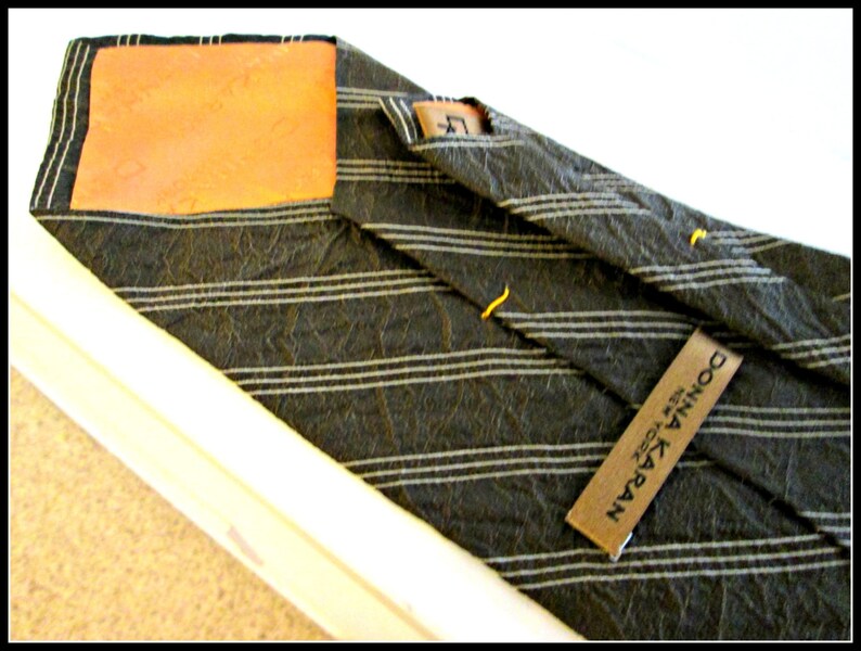 May include: A black and white striped tie with a brown leather patch and a black label that reads "DONNA KARAN NEW YORK".