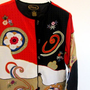 May include: A multi-colored jacket with a black, red, white, and gold pattern. The jacket has a button closure and long sleeves. The fabric has an embroidered design with flowers and swirls. The label on the jacket reads "Allegra".