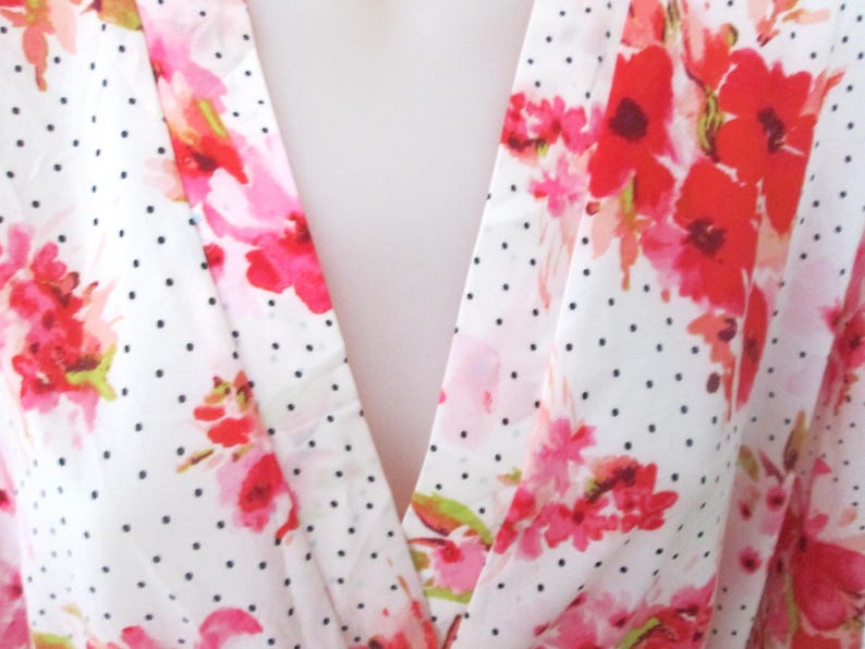 May include: White fabric with a pattern of red and pink floral designs and small black polka dots. The fabric is draped, creating a V-neck shape. The floral pattern is a watercolor style.