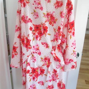 May include: A white robe with a floral pattern featuring red and pink flowers and small black polka dots. The robe has long sleeves and a tie belt. The floral pattern is repeated throughout the garment.