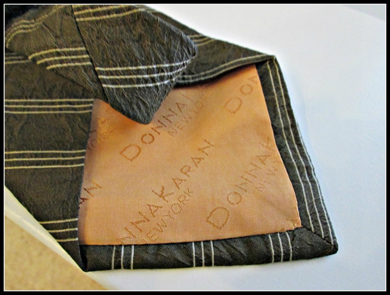 May include: A black and white striped tie with a brown lining. The lining has the text "Donna Karan New York" printed on it.