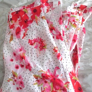 May include: White pajama set with a floral pattern in shades of red and pink, accented with small black polka dots. The set includes a collared top and matching pants, creating a coordinated sleepwear ensemble.