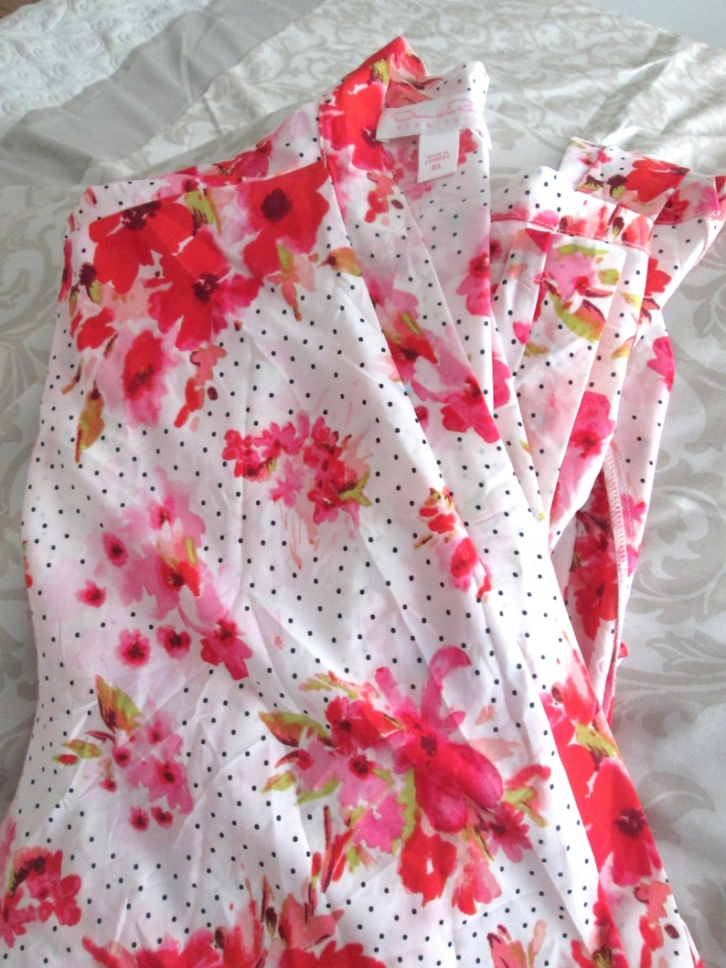 May include: White pajama set with a floral pattern in shades of red and pink, accented with small black polka dots. The set includes a collared top and matching pants, creating a coordinated sleepwear ensemble.