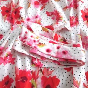 May include: White fabric with a pattern of red and pink flowers and small black polka dots. The fabric is folded, revealing a cuff with the same floral and polka dot design. The overall theme is floral.