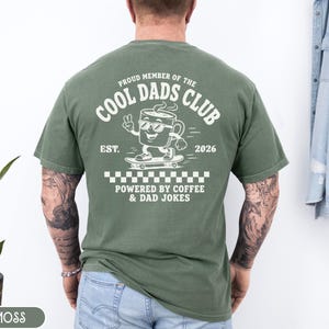 Comfort Colors 1717 Moss t-shirt on male model featuring a white Cool Dads Club coffee mug Powered by Coffee graphic, soft unisex fit, garment dyed cotton texture, vintage washed tee for personalized dad gifts, Father's Day shirts, family style.