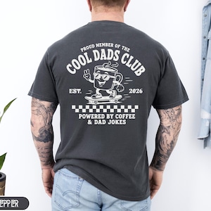 Comfort Colors 1717 Pepper t-shirt on male model featuring a white Cool Dads Club coffee mug Powered by Coffee graphic, soft unisex fit, garment dyed cotton texture, vintage washed tee for personalized dad gifts, Father's Day shirts, family style.
