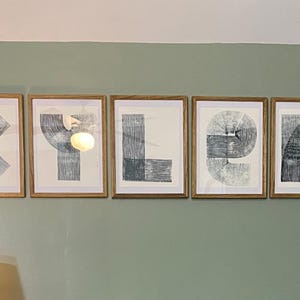 May include: Five framed art prints spelling out the word "KLYER" in a modern, abstract style. Each print features a letter composed of blue and white linear designs within a wooden frame, mounted on a muted green wall.