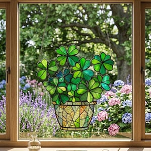 Peut inclure: Suspension de fenêtre en vitrail représentant un pot de trèfles verts. Les trèfles sont de différentes nuances de vert. Le pot est une mosaïque de verre jaune, vert et marron. La fenêtre est dans un cadre en bois, avec un jardin visible à travers le verre.