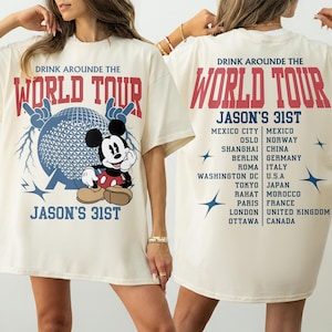 Op de afbeelding: Een off-white t-shirt met een afbeelding van Mickey Mouse, een geodetische bol en de tekst "DRINK AROUNDE THE WORLD TOUR JASON'S 31ST". De achterkant toont een lijst met steden en landen, waaronder Mexico-Stad, Oslo, Shanghai, Berlijn, Rome, Washington DC, Tokio, Rahat, Parijs, Londen en Ottawa.