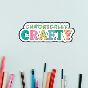 Może przedstawiać: Kolorowa naklejka z napisem "Chronically Crafty" w zabawnym kroju pisma. Naklejka ma białą obwódkę i jest otoczona materiałami rzemieślniczymi, takimi jak długopisy, ołówki i pędzle na jasnoniebieskim tle.