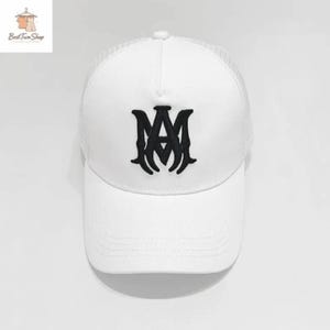 Puede incluir: Gorra de béisbol blanca con parte trasera de malla y visera curva. La gorra presenta un logotipo negro bordado en la parte delantera. Este sombrero de estilo clásico es adecuado para uso casual. El logotipo parece ser las letras "AM" entrelazadas.
