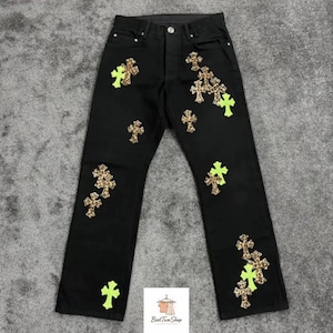 Puede incluir: Vaqueros negros con múltiples parches en forma de cruz. Los parches son una mezcla de estampado de leopardo y verde neón. Los vaqueros tienen un diseño clásico de cinco bolsillos y cierre de botón y cremallera.