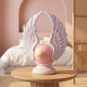 Peut inclure: Une sculpture décorative composée d'une sphère rose centrale ornée d'un emblème en forme d'étoile dorée, flanquée de deux grandes ailes à plumes violet clair. L'ensemble repose sur une base incurvée lisse avec des détails de lignes gravées.