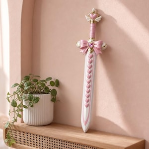 May include: A decorative sword featuring a pink and white color scheme with a heart-shaped pommel, small white wings, a large pink bow at the crossguard, and a series of pink heart accents running down the center of the white blade.