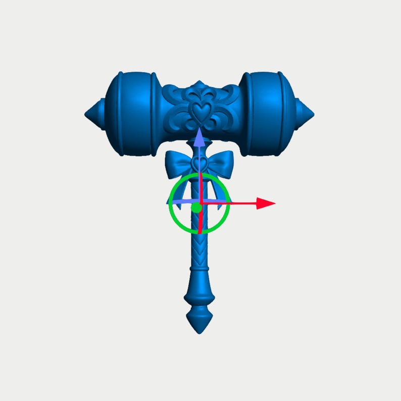 Op de afbeelding: Een felblauw 3D-digitaal model van een hamer met een hartvormig embleem op de kop, een strikdetail bij de nek en een textuur op het handvat. Een groen cirkelvormig transformatie-gizmo met rode, blauwe en groene pijlen is gecentreerd.