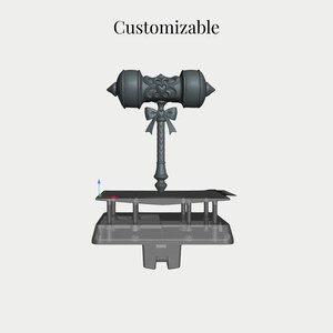 Op de afbeelding: Een grijs 3D digitaal model van een hamer met een hartvormig embleem op de kop en een strikdetail op het handvat. Het woord Customizable staat boven het object, dat op een platform met een basissteunstructuur is geplaatst.
