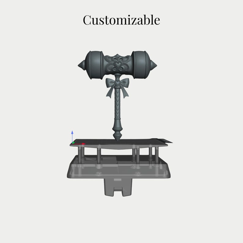 Op de afbeelding: Een grijs 3D digitaal model van een hamer met een hartvormig embleem op de kop en een strikdetail op het handvat. Het woord Customizable staat boven het object, dat op een platform met een basissteunstructuur is geplaatst.