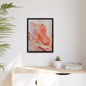Peut inclure: Impression d'art abstrait dans un cadre noir. L'œuvre présente d'épaisses touches de pinceau dans des tons de rose, de pêche et de blanc, créant un effet de texture en empâtement. La peinture est exposée sur un mur blanc au-dessus d'un meuble en bois.