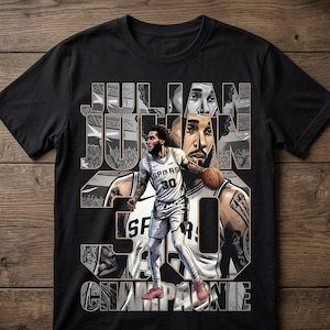 May include: Black t-shirt featuring a graphic of a basketball player with the name "JULIAN CHAMPAGNE" and the number "30". The design includes illustrations of the player in action, with a basketball and a crowd in the background.
