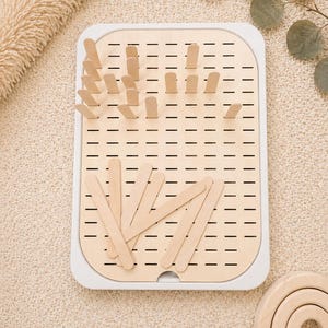 Può includere: Uno scolabiberon in legno con cornice bianca e interno in legno chiaro. Il portabiberon ha diversi pioli in legno e fessure per asciugare biberon e accessori. Sono inclusi anche diversi bastoncini di legno.