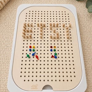 Può includere: Un gioco da tavolo con pioli in legno con una cornice bianca. La tavola ha numerosi fori e pioli in legno che compongono la parola "Etsy". I pioli colorati sono sparsi sulla tavola. Il logo LaserLux è visibile.