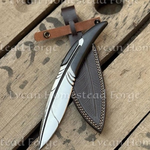 Puede incluir: Un cuchillo de hoja fija con una hoja de metal plateado en forma de pluma, con un mango oscuro y una funda de cuero marr&oacute;n oscuro a juego con detalles de plumas en relieve y una correa de cuero con botones de presi&oacute;n de metal.