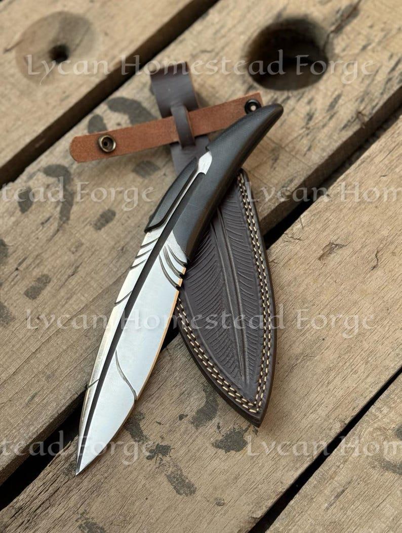 Puede incluir: Un cuchillo de hoja fija con una hoja de metal plateado en forma de pluma, con un mango gris oscuro y una funda de cuero marr&oacute;n oscuro a juego con detalles de plumas en relieve y un cierre de correa con bot&oacute;n a presi&oacute;n.