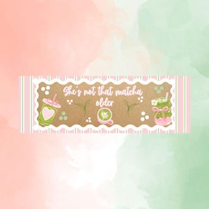 May include: A rectangular sticker with a scalloped white border and pink striped edges. The center features the text 'She's not that matcha older' in white, surrounded by illustrations of green matcha drinks, tea leaves, and small white dots.