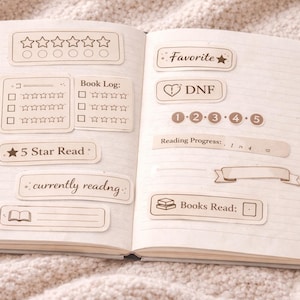 Könnte beinhalten: Offenes Notizbuch mit Aufklebern zur Buchverfolgung. Aufkleber enthalten Bewertungssterne, ein Buchprotokoll, "Favorite", "DNF", die Zahlen 1-5, "Reading Progress", "5 Star Read", "currently reading" und "Books Read".